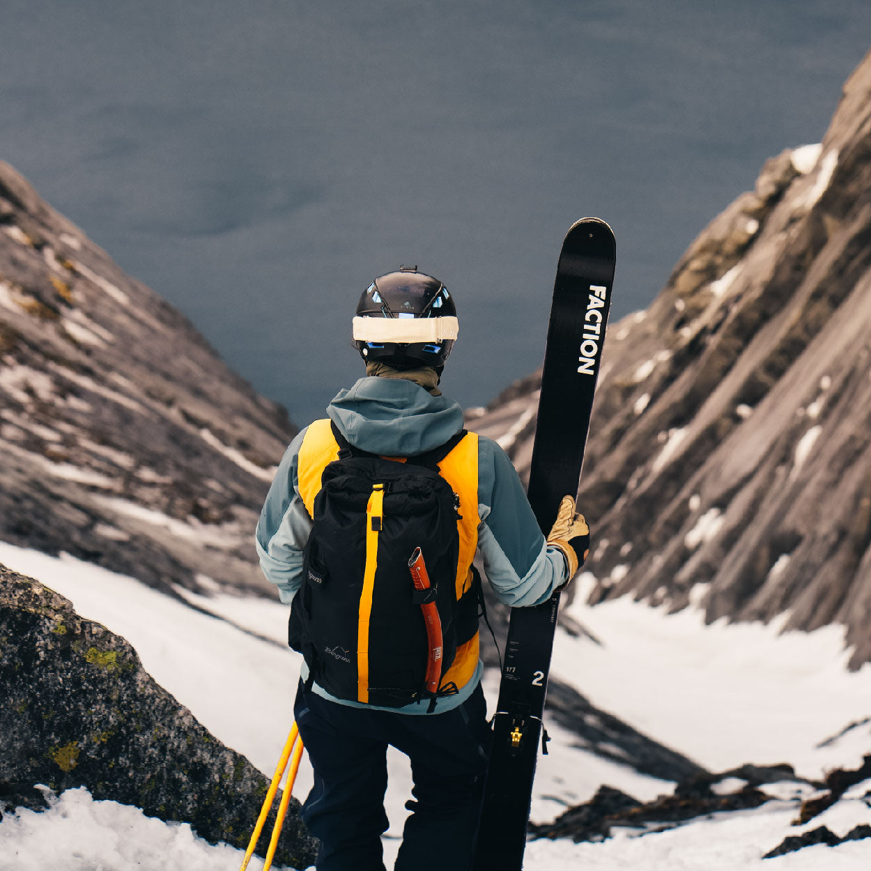 Skier holding skis looking over fjord. 