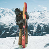Young skier holding Faction Dancer Grom red skis in a snowy alpine setting.
